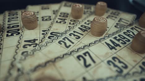 Crane-shot-of-a-Bingo-desk-lottery-game,-vintage-cards-with-numbers,-wooden-chips,-super-slow-motion-120-fps,-studio-lights