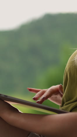 lady in green blouse works on thin laptop computer sitting against distant mountains at eco resort hotel close side view zoom in slow motion