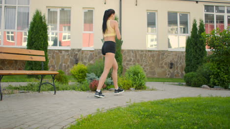 a woman makes lunges on a sidewalk path in a park in an urban environment. slow-motion shooting of a woman in sportswear steps with a lunge