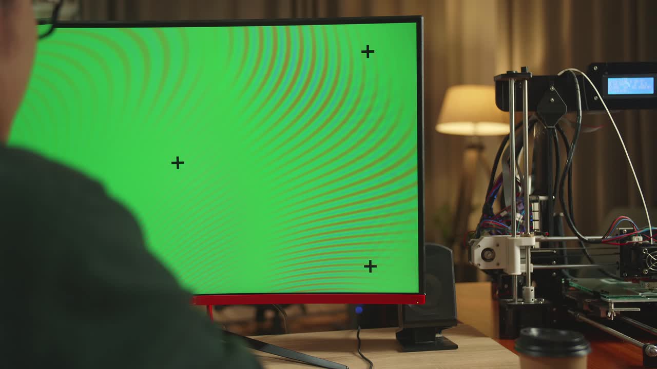 Person using a computer with a green screen and 3D printer