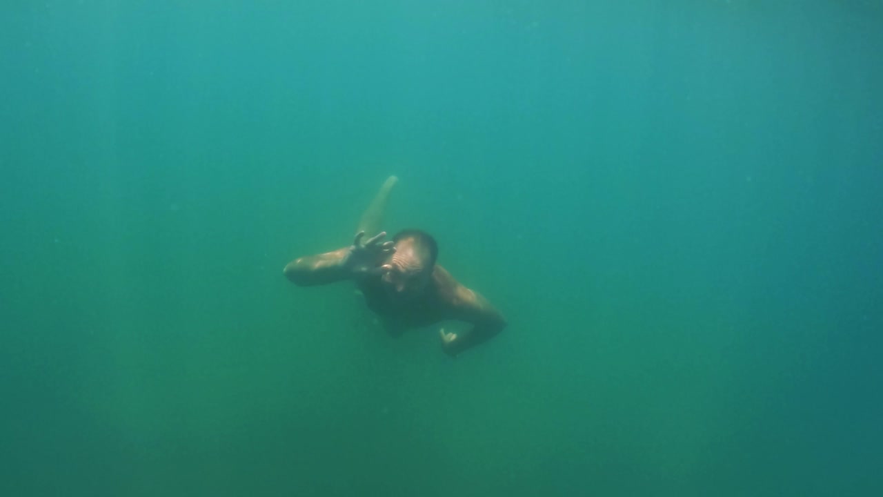 Undersea scene of adult man in apnea swimming toward camera while smiling