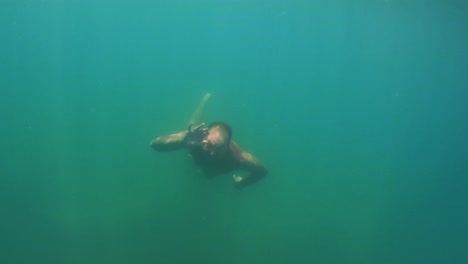 undersea scene of adult man in apnea swimming toward camera while smiling