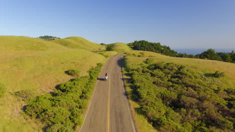 Una-Motocicleta-Conduciendo-A-Lo-Largo-De-Una-Pintoresca-Carretera-Rural-A-Lo-Largo-De-Verdes-Colinas-Cubiertas-De-Hierba-Cerca-De-Mt-Tamalpais,-California---Sobrevuelo-Aéreo