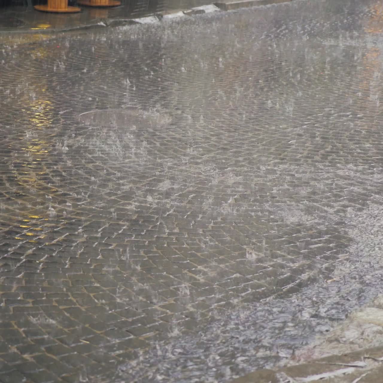rain drops are falling on the road in the city. Water are flowing by a stream on the wet pavement