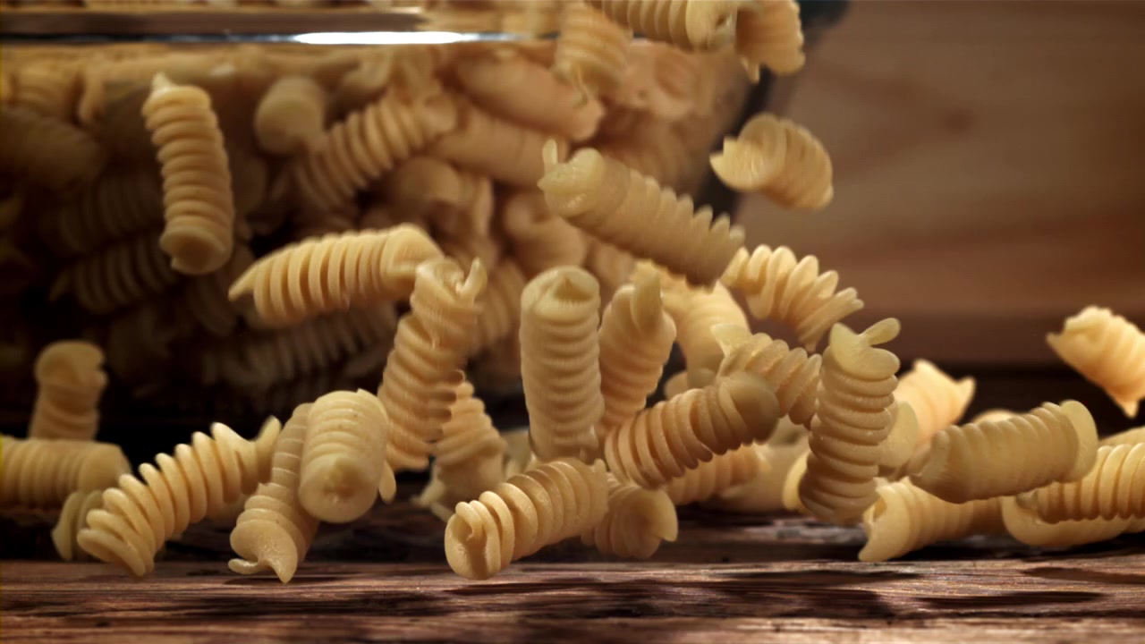Pasta fusilli cruda che cade al rallentatore su una superficie di legno.