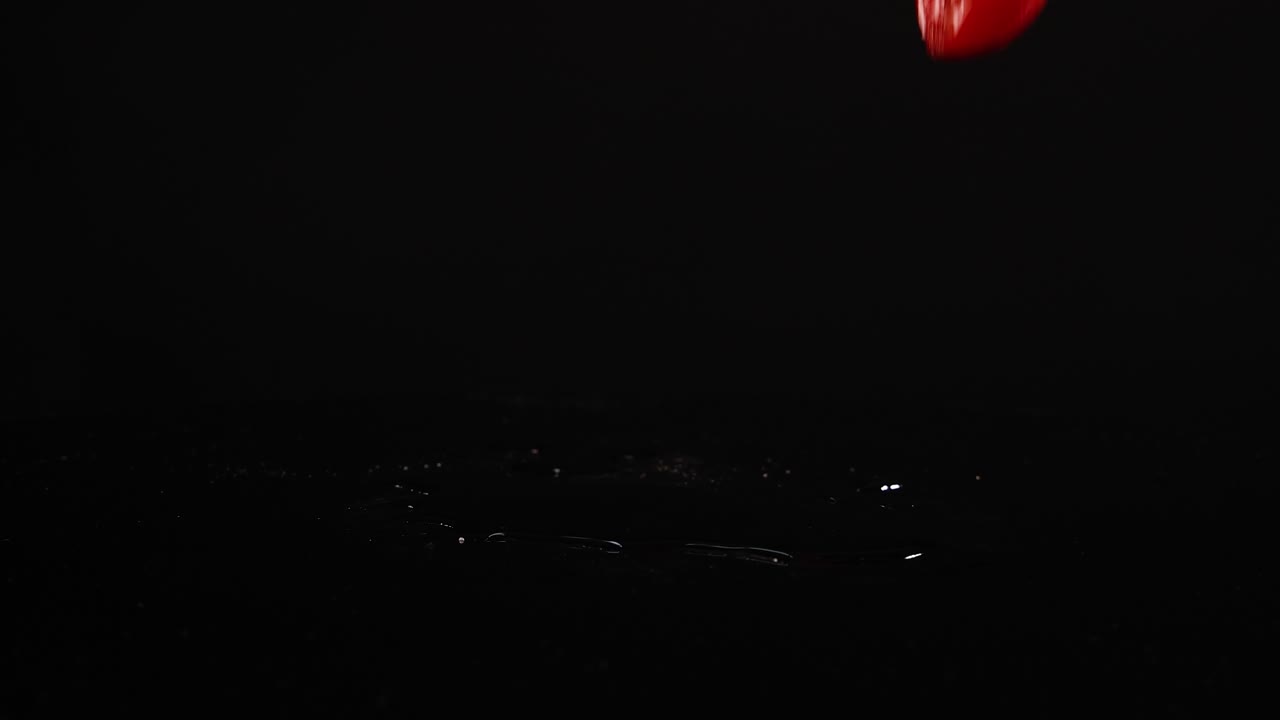 Cherry tomatoes fall and bounce on a reflective black surface, captured in slow motion with dramatic lighting