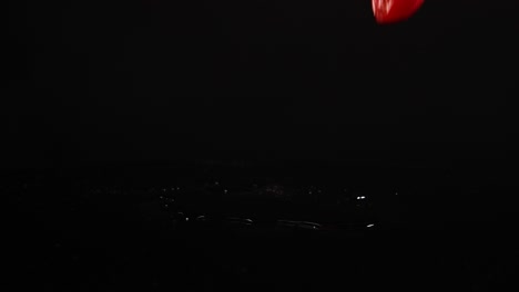 cherry tomatoes fall and bounce on a reflective black surface, captured in slow motion with dramatic lighting