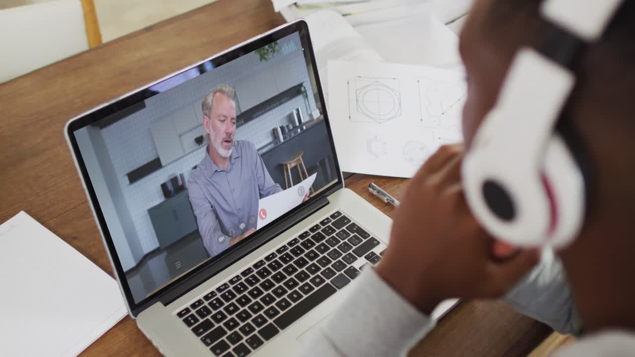 African american businessman sitting at desk using laptop having video call with male colleague