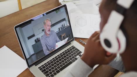 African-american-businessman-sitting-at-desk-using-laptop-having-video-call-with-male-colleague