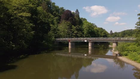 Car-crossing-a-narrow-bridge-that-reflects-perfectly-in-the-flat-brown-river-water-underneath