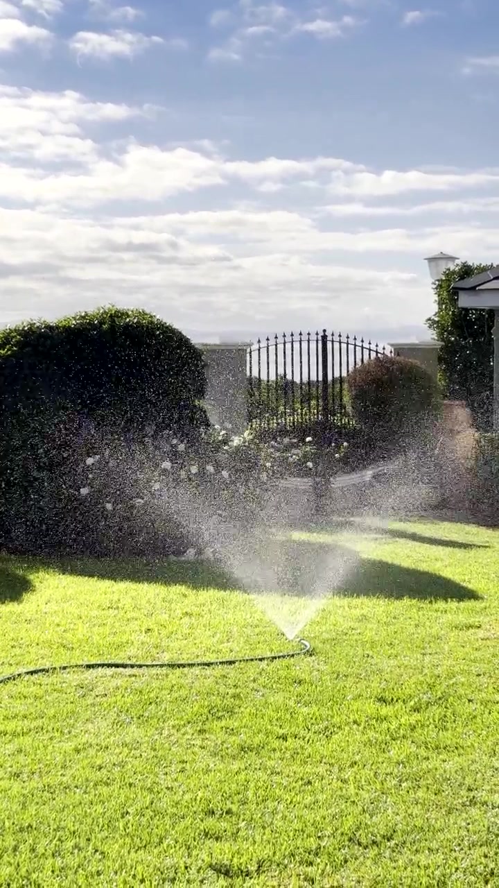 Irrigatore che irriga un prato lussureggiante nel giardino anteriore di una casa, verticale