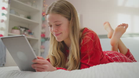 teenage girl wearing orthodontic braces lying on bed at home streaming movie onto digital tablet and laughing - shot in slow motion