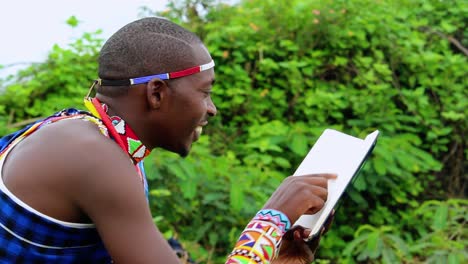 hombre masai feliz, sentado en un bosque, leyendo un libro, en áfrica