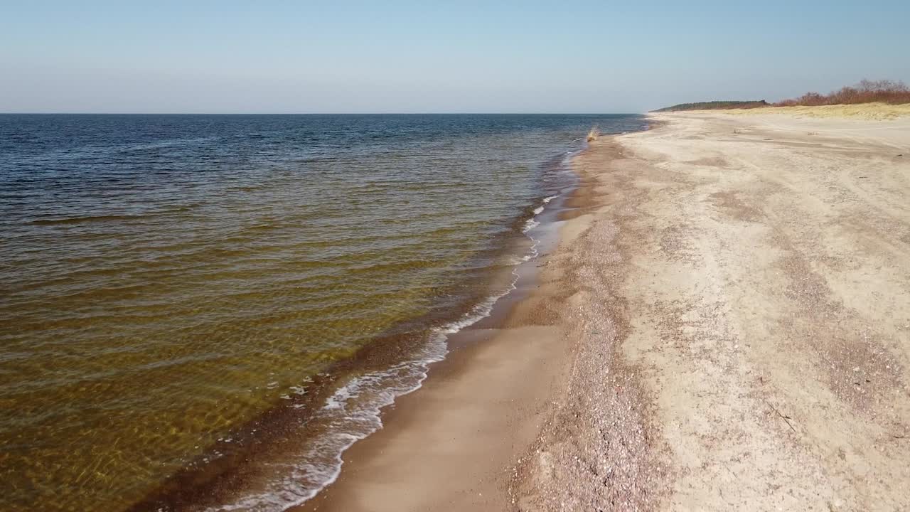Widok z lotu ptaka na fale morskie rozbijające się o plażę z białym piaskiem w słoneczny wiosenny dzień, Morze Bałtyckie, plaża Pape, Łotwa, szerokokątne ujęcie z drona wznoszącego się