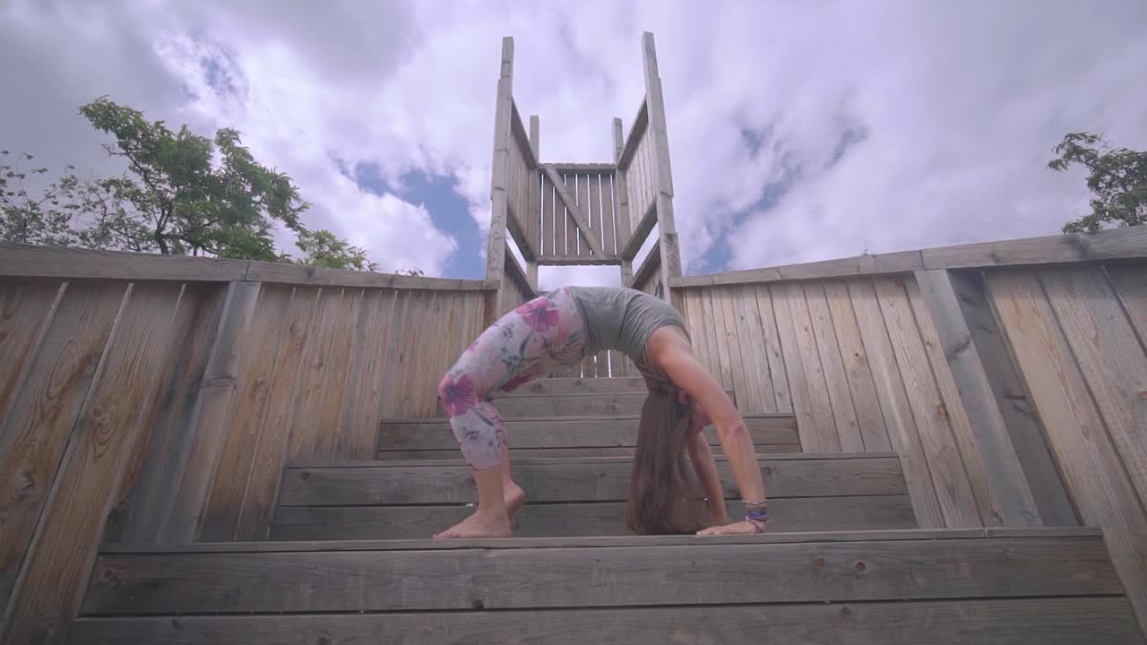 mujer atlética en posición de chakrasana levantando lentamente su pierna derecha - yoga en una escalera de madera abierta - ángulo bajo, cámara lenta