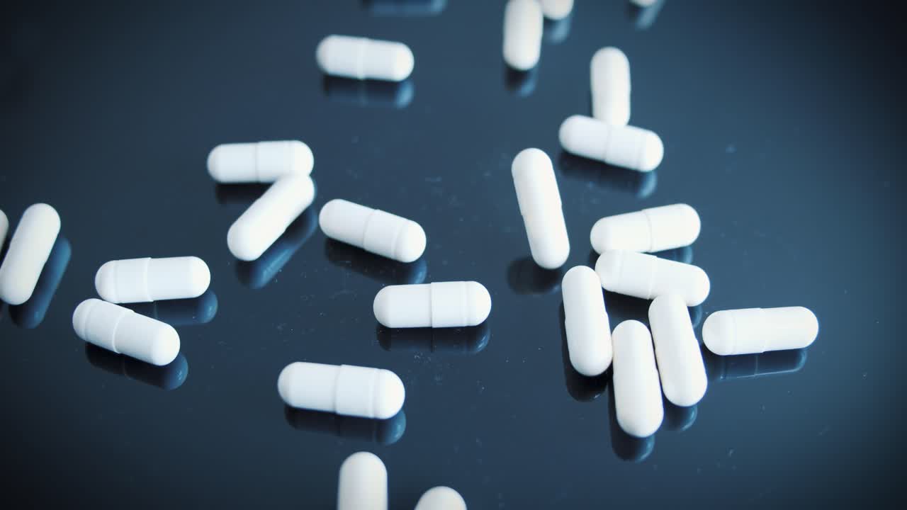 흰색 의료용 알약이 검은색 반사 표면에 떨어집니다.