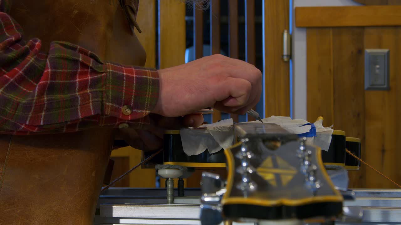 Closeup detail: Guitar tech in shop fills chips in electric guitar neck