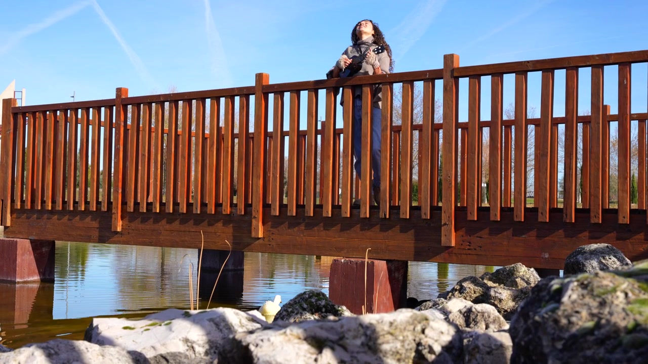 Giovane donna che suona l'ukulele e canta felicemente su un ponte di legno su un lago in una giornata di sole