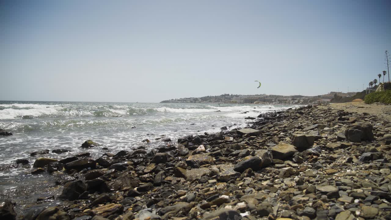 A pan up from rocky beach looking toward Cala De mijas as a Kite surfer sails in distance