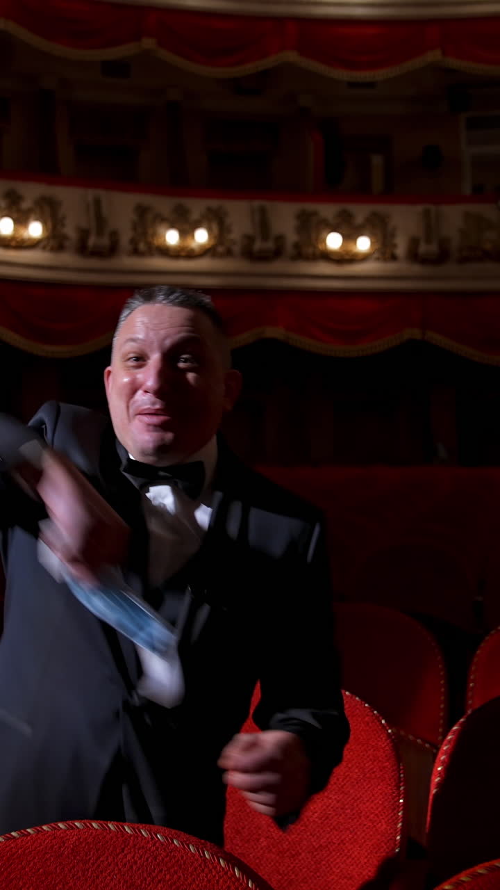 Happy actor puts off medical mask and throws it. Man in costume sitting in the empty theatrical hall and invites joyfully to come to performance. The end of pandemic. Vertical video