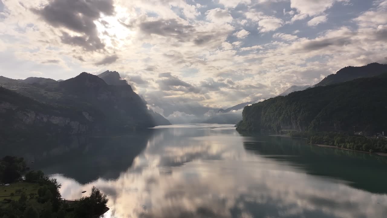 Dramatic aerial view of Walensee in Switzerland with mountains reflecting on the still lake under a cloudy, glowing sky capturing natural beauty and serene landscape