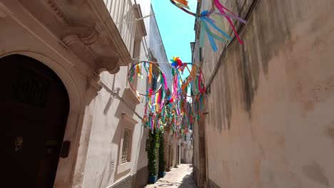 Walking-on-the-streets-under-some-colourfull-décoration-or-art-in-Martina-Franca,-Italia-by-a-sunny-day