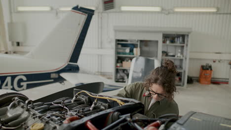 female mechanic repairing aircraft engine with wrench in aviation hangar