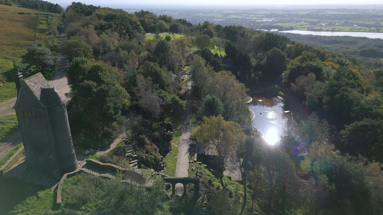돌로 지어진 탑 건물은 가을에 나무들 사이에 있는 연못에서 반사되는 빛을 가진 테라스 정원입니다.