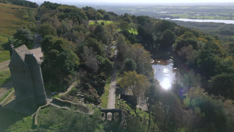 stone tower building and terraced gardens with sunlight reflecting from pond amongst trees in autumn