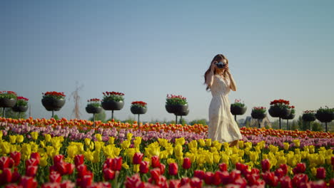 una joven con una cámara tomando fotos de hermosos tulipanes. una chica caminando por el parque.