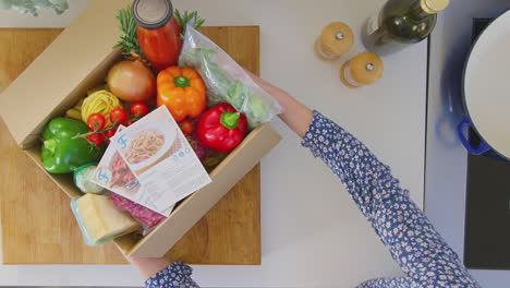 View from above of woman with recipe cards and box of delivered fresh ingredients planning meal - shot in slow motion