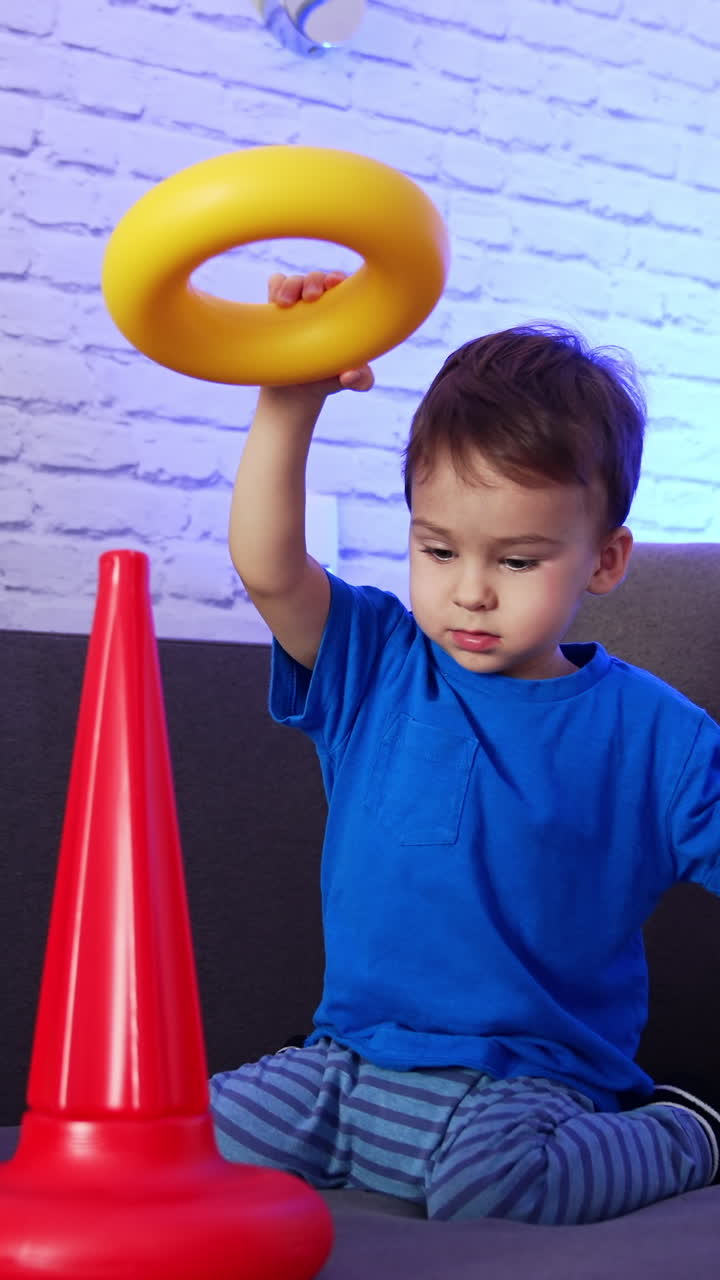 Little kid playing with pyramid on the sofa. Happy active toddler disassembling the toy and rejoicing. Vertical video