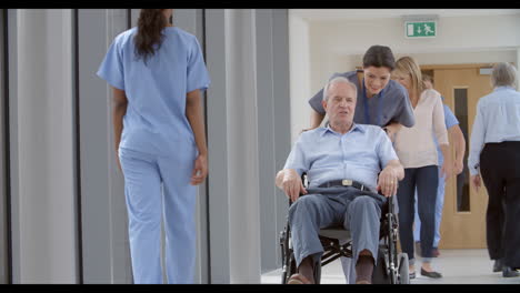 Nurse-Pushing-Senior-Patient-In-Wheelchair-Along-Corridor