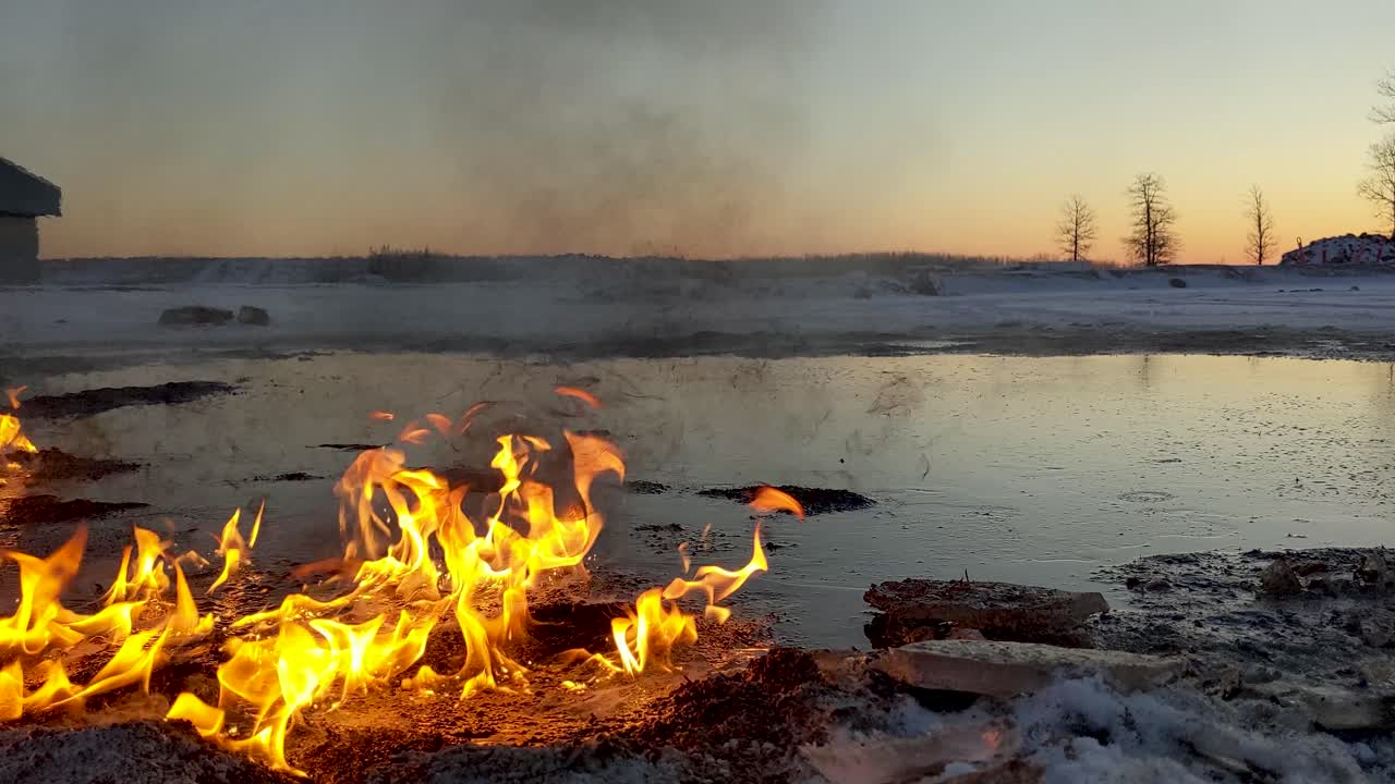 An oil spill slowly burning among the melted snow.  Sun rises in background