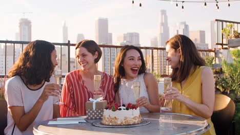 portrait of female friends celebrating birthday on rooftop terrace with city skyline in background