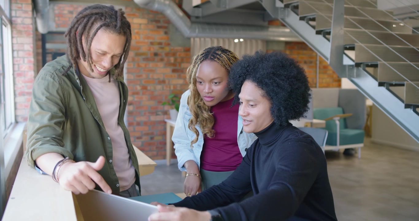 Afroamerikanske kolleger samarbejder ved et ståbord, en kollega læner sig ind og gennemgår en bærbar computer.