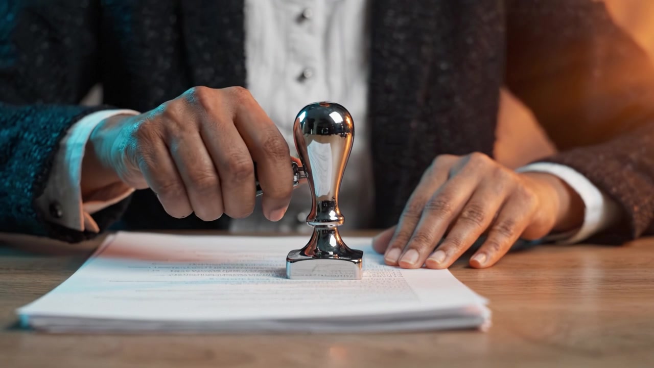 A Professional Individual Applying a Notary Seal to Official Documents on a Wooden Desk with a Focus on the Commitment to Authenticity and Legal Validation