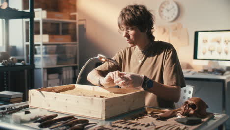 focused female archaeologist cleaning artifact with brush in sand tray