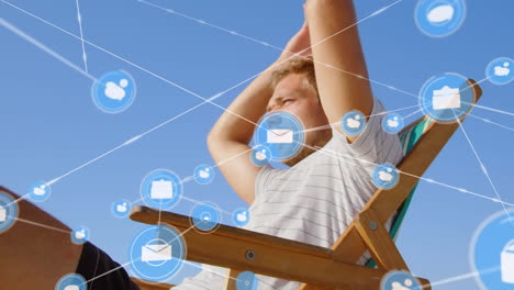 animation of network of connections with icons over man in deckchair on beach