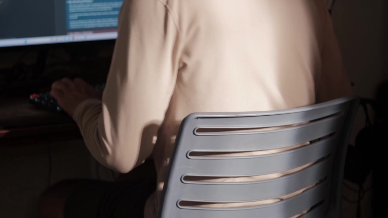Inquadratura statica da dietro di un giovane seduto a una scrivania per usare un computer prima di alzarsi e andarsene.