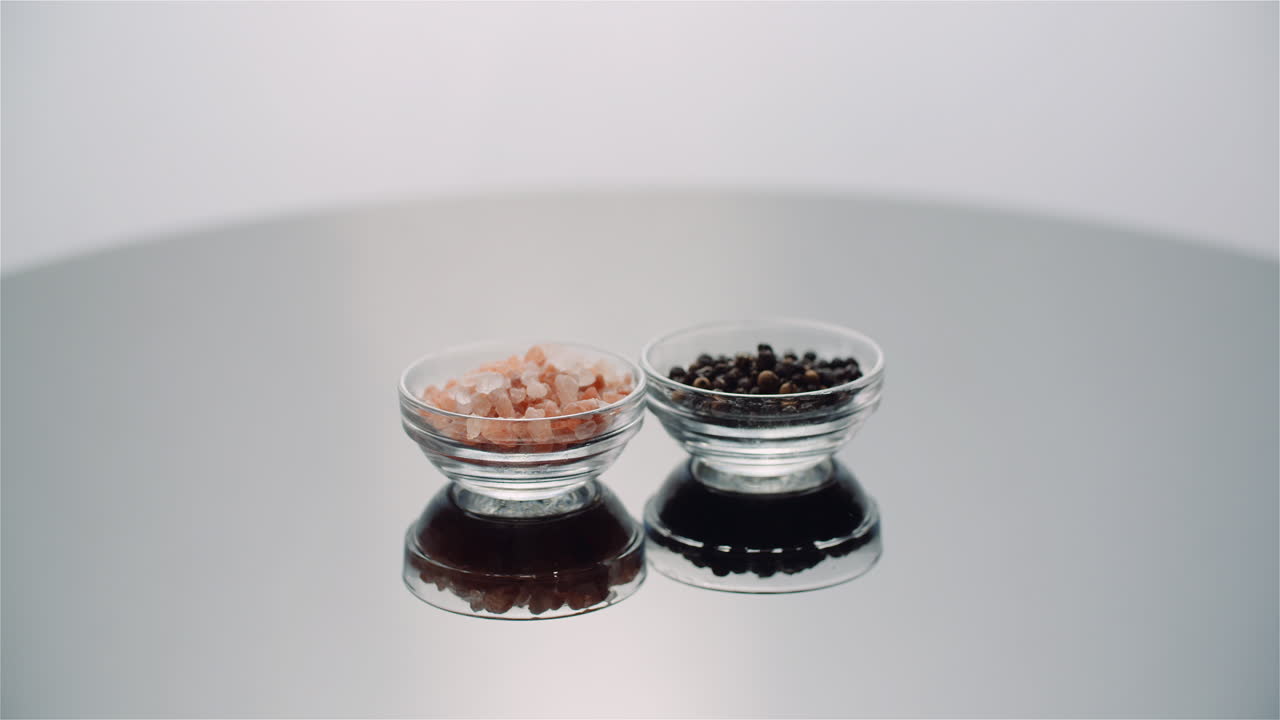 Himalayan Salt and Black Peppercorns in Bowls on Reflective Surface