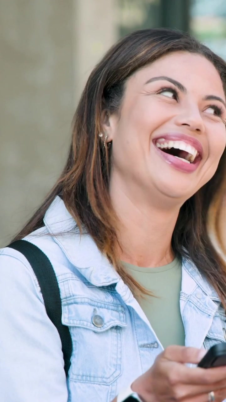 Video vertical: Mujer sonriente con chaqueta vaquera leyendo una alerta en el teléfono en la acera de la ciudad, sosteniendo una taza de café
