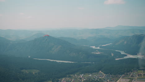 Paraglider-flies-over-large-green-valley-at-mountains-feet