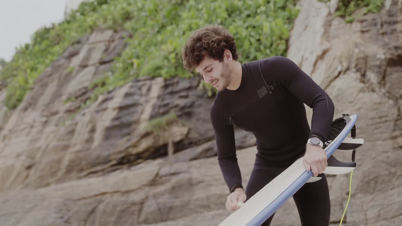 Man in wetsuit with surfboard at a rocky beach
