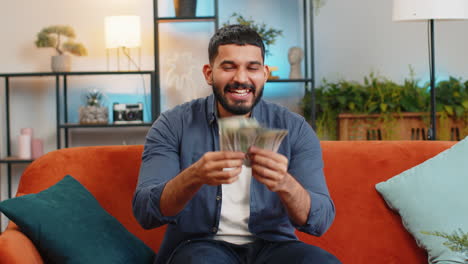 Excited-happy-Indian-man-showing-money-dollar-cash-bills-satisfied-of-income-saves-salary-earnings