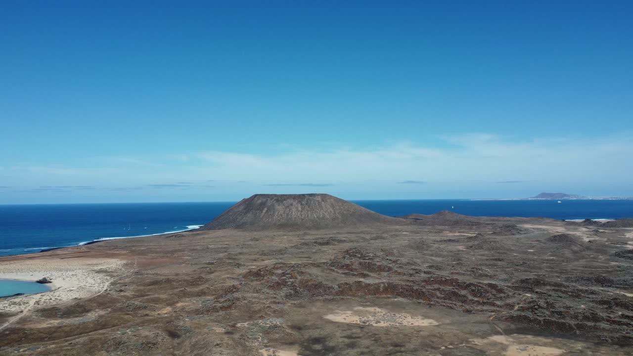 작은 산을 향해 울퉁불퉁한 지형을 날아갈 때 아름답고 맑고 푸른 하늘을 보여주는 스페인의 늑대 섬의 공중 전망
