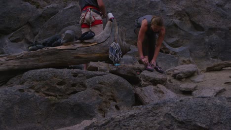 the camera tilts up to reveal two rock climbers preparing at the base of a rock wall