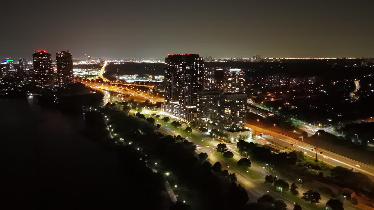 Forward drone shot over illuminated Parklawn buildings and traffic at night Toronto