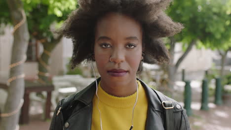 portrait of cool trendy african american woman student with funky afro looking serious at camera listening to music wearing earphones