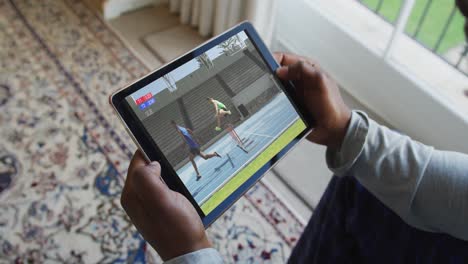 compuesto de un hombre sentado en casa viendo un evento de atletismo en una tableta